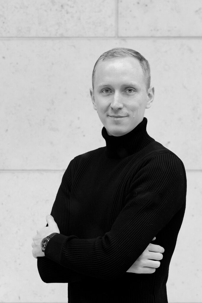 Porträt eines Mannes mit verschränkten Armen, der einen schwarzen Rollkragenpullover trägt und in die Kamera schaut. Es ist Stefan Panait.