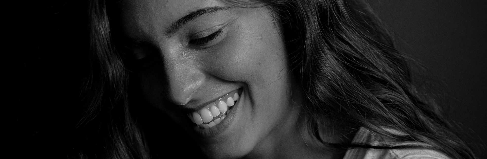 Lächelnde Frau mit langen, lockigen Haaren und strahlenden Zähnen in einem Schwarz-Weiß-Porträt.