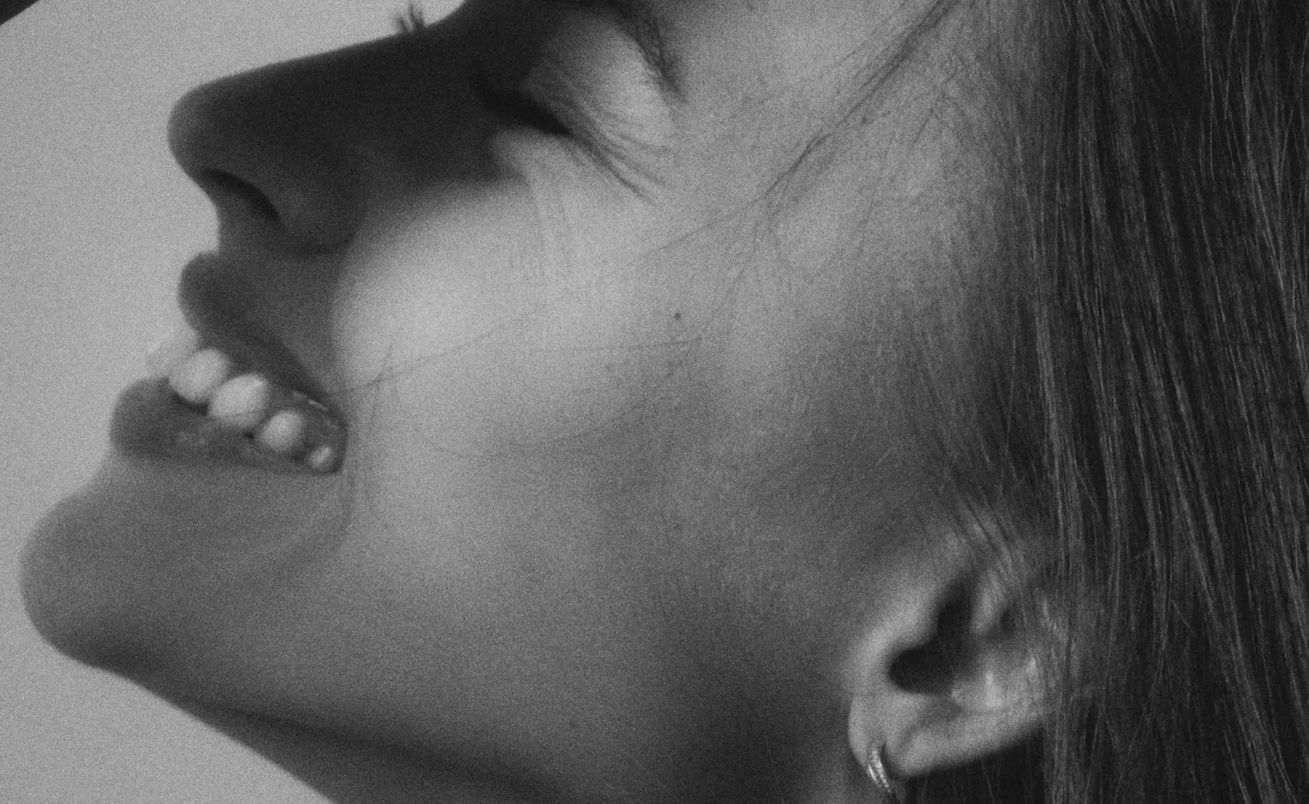 Nahaufnahme eines lächelnden Gesichts mit geschlossenen Augen und langen Haaren, das eine positive Emotion ausstrahlt.