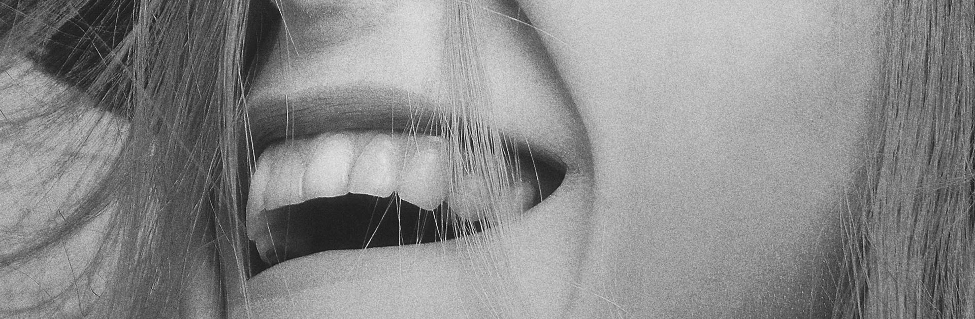 Nahaufnahme eines lächelnden Gesichts mit sichtbaren Zähnen und Haaren, die sanft über die Wange fallen.