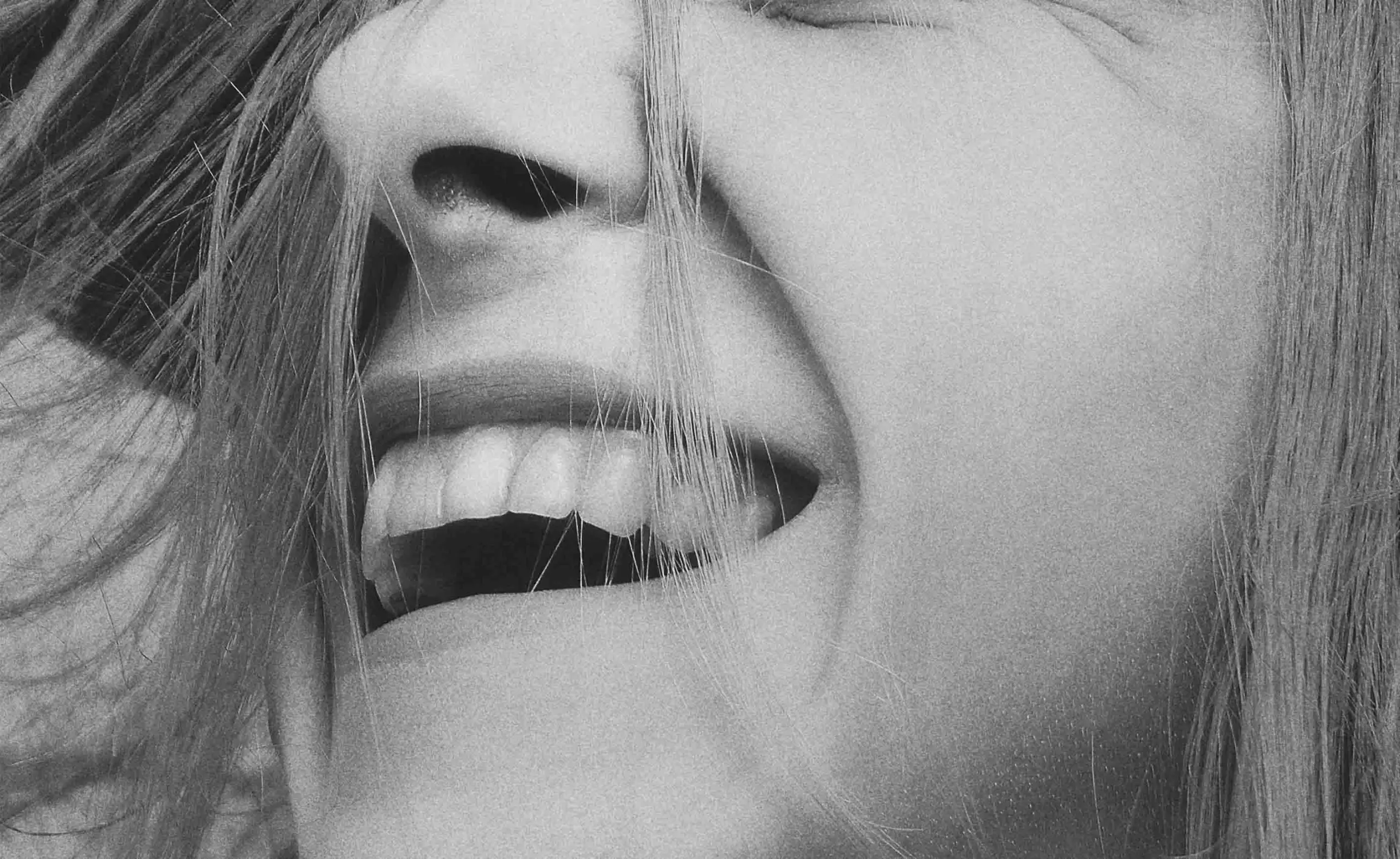 Nahaufnahme eines lachenden Gesichts mit sichtbaren Zähnen und Haaren, die im Wind wehen.