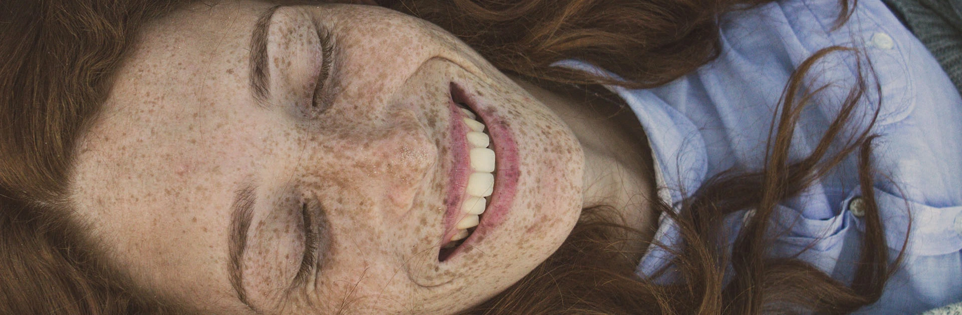 Lächelnde Frau mit roten Haaren und Sommersprossen, die auf dem Rücken liegt und die Augen geschlossen hat.