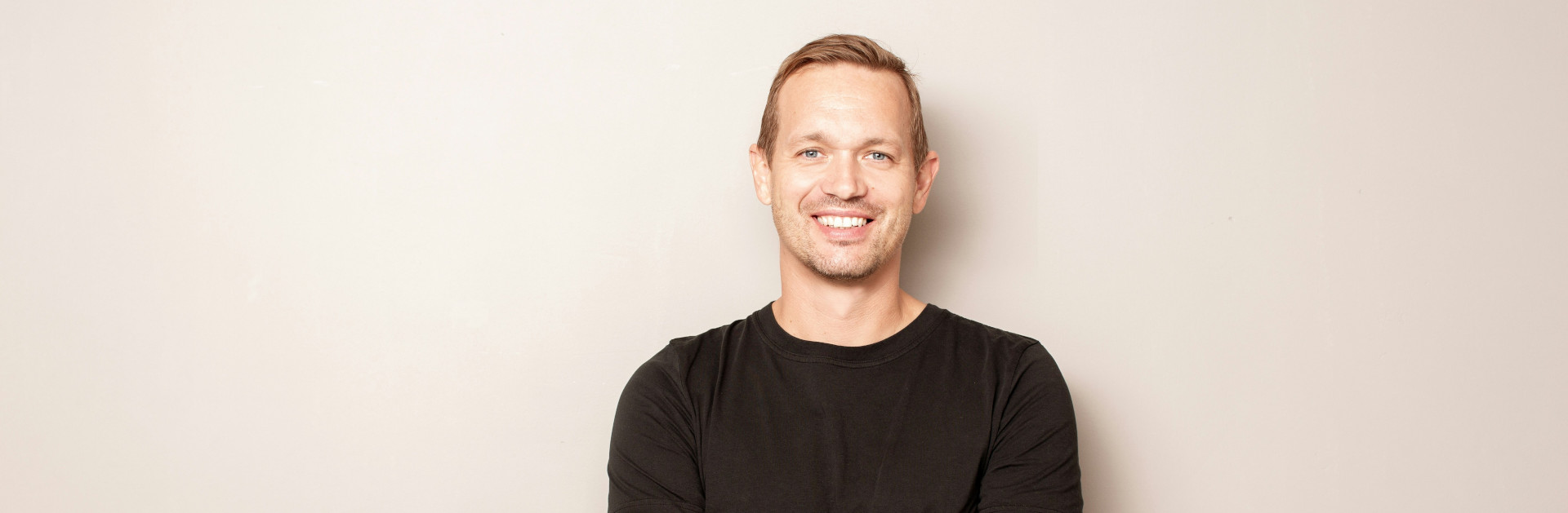 Portrait eines Mannes in schwarzem T-Shirt vor beiger Wand; Kontext SP64 Contemporary Dentistry, Implantologie im Frankfurter Westend, Frankfurt.