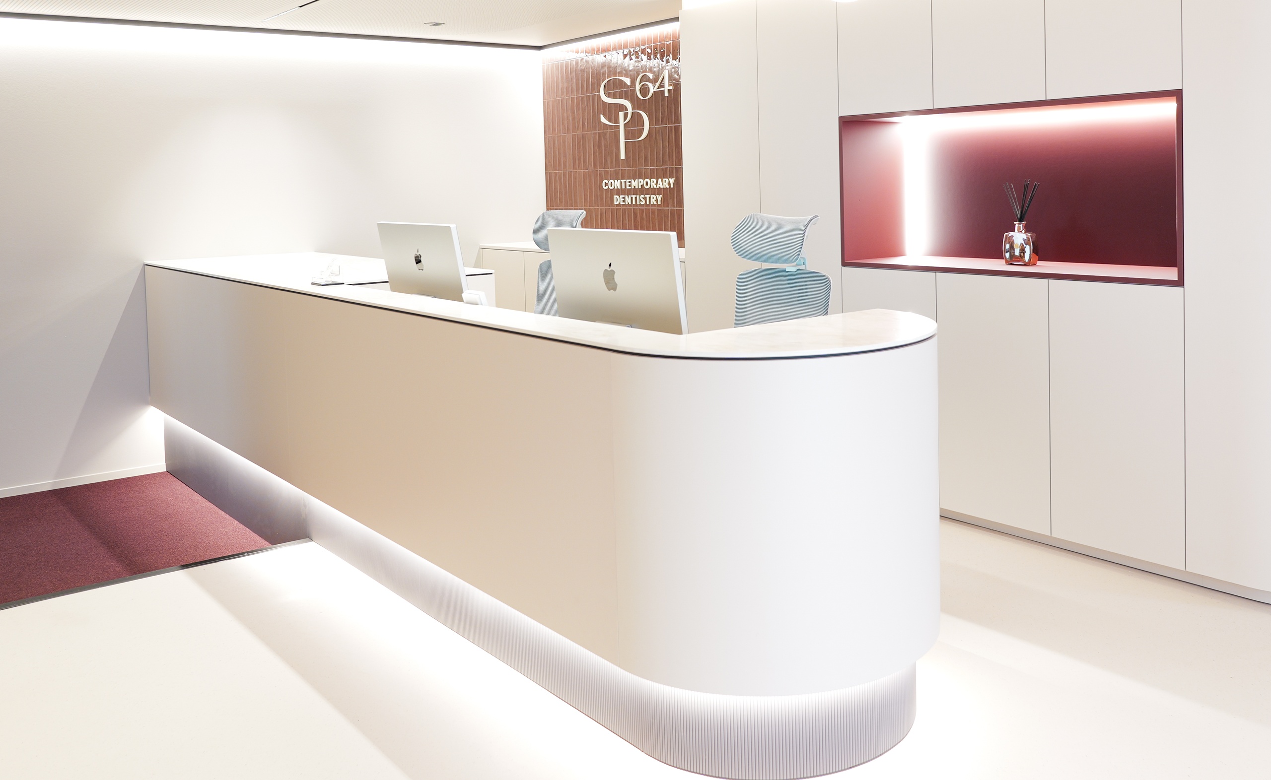 Weiße, moderne Empfangstheke im Look von SP64 – Contemporary Dentistry, mit roter Lichtinszenierung und S64-Logo für Frankfurt-Bockenheim.